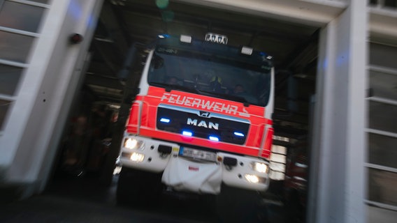 Ein Feuerwehrfahrzeug in Unschärfe fährt aus dem Hallentor einer Feuerwache. © NDR Foto: Julius Matuschik