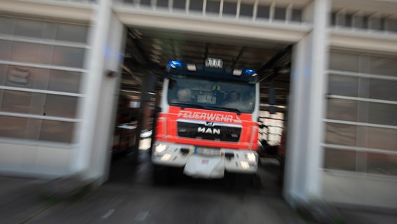 Ein Feuerwehrfahrzeug in Unschärfe fährt aus dem Hallentor einer Feuerwache. © NDR Foto: Julius Matuschik