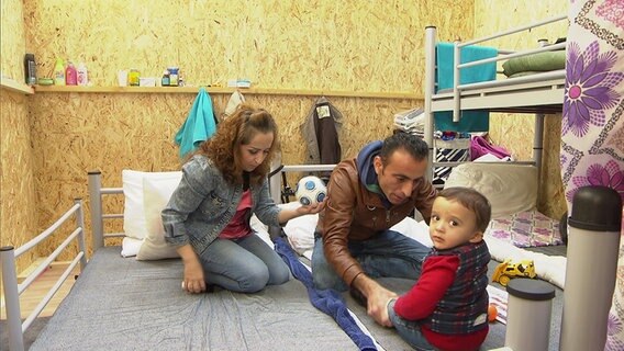 Eine Familie sitzt in einer Flüchtlingsunterkunft auf einem Bett. © NDR Foto: Nadia Yaqub