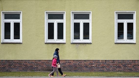 Eine Frau und ein Kind gehen vor einer Flüchtlingsunterkunft vorbei. © picture alliance/dpa Foto: Holger Hollemann