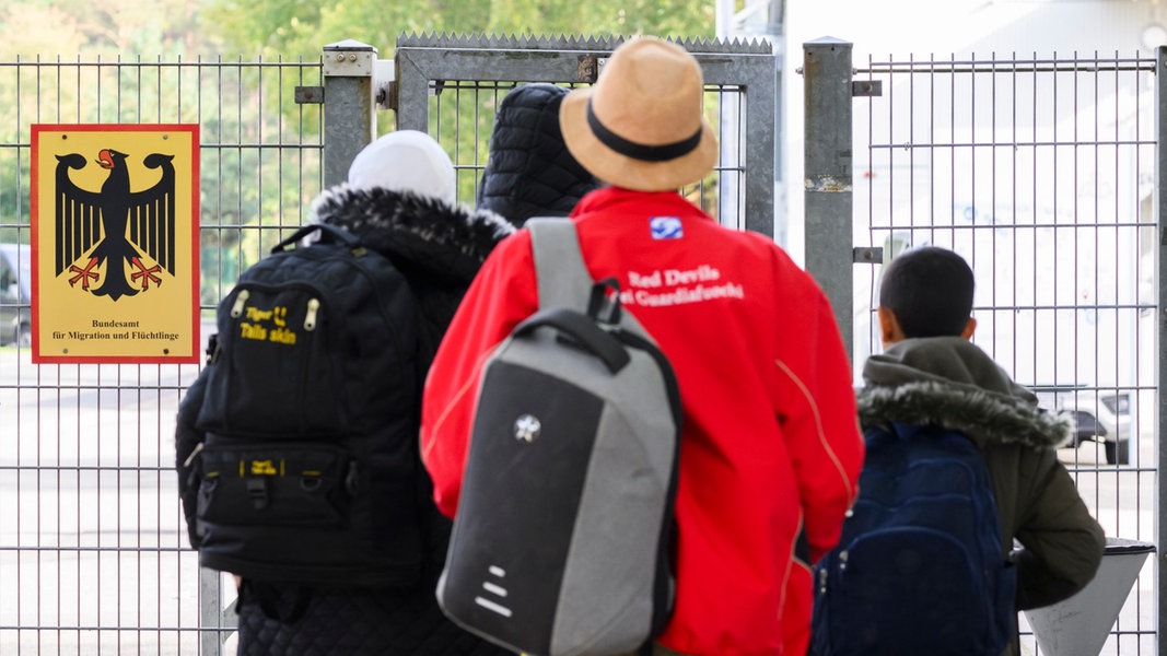 Geflüchtete betreten neben einem Schild vom Bundesamt für Migration und Flüchtlinge die Landesaufnahmebehörde Niedersachsen am Standort Braunschweig