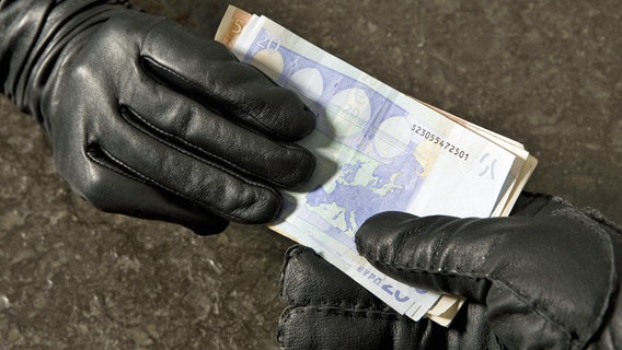Euroscheine wechseln von einer Hand in schwarzem Lederhandschuh zu einer anderen. © blickwinkel/picture alliance Foto: McPHOTOs