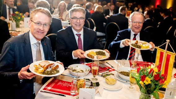 Der neue Oldenburger Grünkohlkönig Daniel Günther (CDU), Ministerpräsident von Schleswig-Holstein, und Jürgen Krogmann (SPD), Oberbürgermeister der Stadt Oldenburg, und Stephan Weil (SPD), Ministerpräsident von Niedersachsen, halten ihre Teller mit einer Portion Grünkohl in die Kamera. © dpa Foto: Hauke-Christian Dittrich