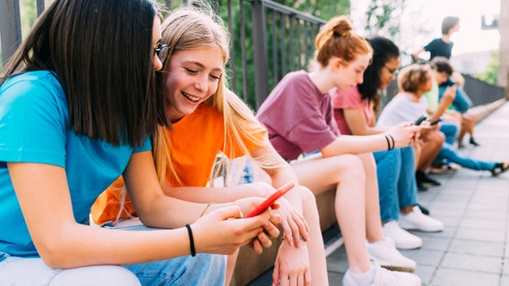 Schüler sitzen auf einer Mauer und schauen auf ihre Smartphones. © picture alliance / Westend61 | Eugenio Marongiu Foto: Eugenio Marongiu