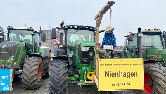 An einem Traktor ist Galgen mit einer Strohpuppe befestigt. An der Puppe ist ein Schild mit "Bauer" und einem Kreuz. © NDR Foto: Tanja Niehoff