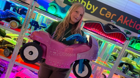 Eine Frau hält ein lackiertes Bobbycar in einer Ausstellung. © NDR Foto: Barbara Kreuzer