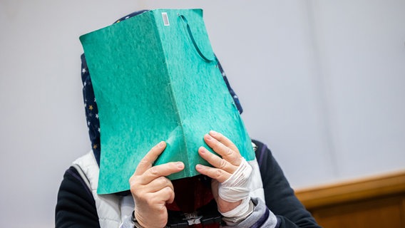Die Angeklagte (l) steht vor Prozessbeginn in einem Gerichtssaal im Landgericht Bückeburg neben ihrem Anwalt Thilo Schäck (r) und hält sich eine Dokumentenmappe vor ihr Gesicht. © picture alliance/dpa Foto: Michael Matthey