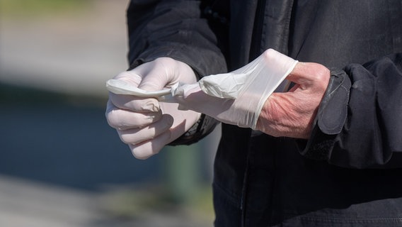 Ein Mann in Hannover zieht sich Plastikhandschuhe an. © dpa - Bildfunk Foto: Julian Stratenschulte