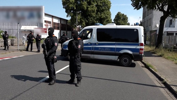 SEK Beamte stehen vermummt vor einem Einsatzfahrzeug der Polizei. © Screenshot 