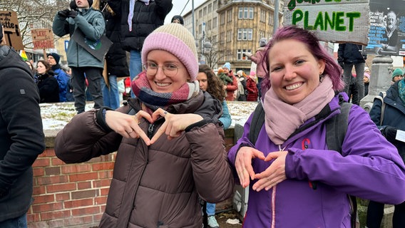 Zwei junge Frauen sind auf einer Demonstration und formen ein Herz mit ihren Händen. © NDR Foto: Kristina Hoffmann