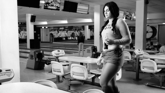 Eine Frau hat eine Cola-Flasche in der Hand und geht in einem Bowling-Center auf einen Tisch zu. © Hochschule Hannover Foto: Benjamin Zvonar