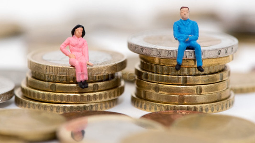 Die Figuren eines Mannes und einer Frau sitzen auf Stapeln aus Geldmünzen (gestellte Szene).