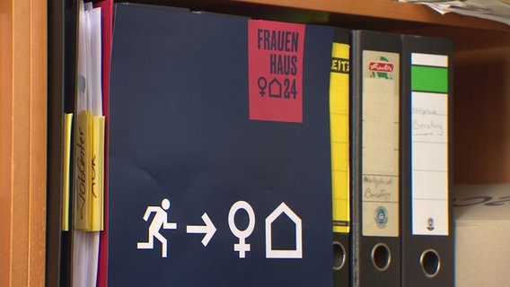 An Ordnern in einem Regal lehnt ein Papier mit dem Logo des Frauenhauses. © NDR 