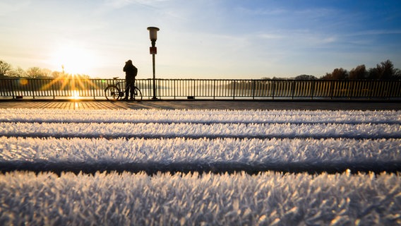 Mit Raureif bedeckt ist bei Sonnenaufgang eine Sitzbank am Maschsee. © Julian Stratenschulte/dpa Foto: Julian Stratenschulte