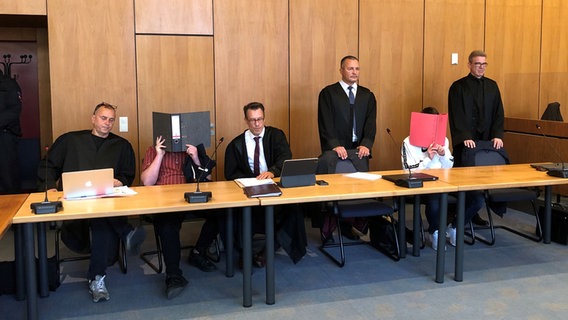Die Angeklagten in einem Prozess um einen Gullydeckel-Wurf auf die Autobahn 7 stehen mit ihren Anwälten vor Gericht. © NDR Foto: Marie Gottschalk