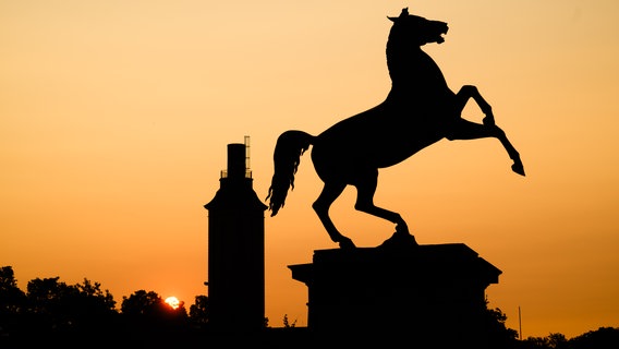 Die Silhouette des Sachsenrosses vor dem Welfenschloss der Leibniz Universität Hannover zeichnet sich vor dem Sonnenaufgang verfärbten Morgenhimmel ab. © picture alliance/dpa Foto: Julian Stratenschulten