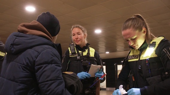 Das Bild zeigt zwei Polizistinnen bei der Kontrolle einer Person. © NDR 