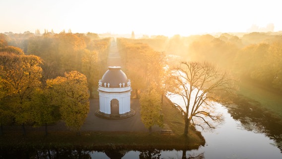 Die aufgehende Sonne taucht Nebelschwaden über einen der Eckpavillons des französischen Architekten Remy de la Fosse in den Herrenhäuser Gärten in goldenes Licht. © Julian Stratenschulte/dpa Foto: Julian Stratenschulte