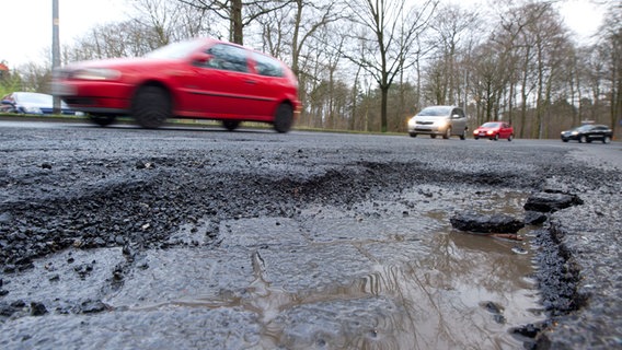 Autos fahren an einem Schlagloch auf einer Straße vorbei. © dpa-Bildfunk Foto: Sebastian Kahnert