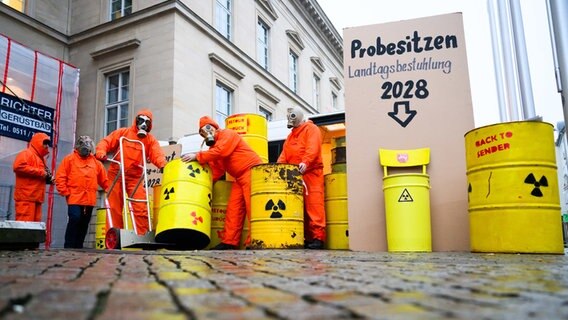 Demonstranten der Bürgerinitiative Strahlenschutz BISS Leese stehen mit künstlichen Atommüllfässern vor dem niedersächsischen Landtag. © dpa Foto: Julian Stratenschulte