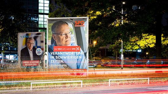 Wahlplakate zeigen am frühen Morgen Bernd Althusmann (CDU, l) und Stephan Weil (SPD, r) während Autos eine Hauptstraße entlang fahren. © dpa-Bildfunk Foto: Moritz Frankenberg/dpa