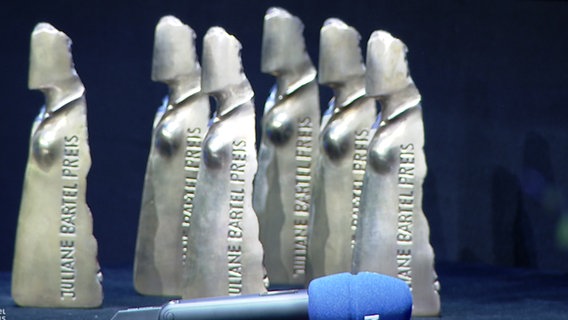 Trophäen zum Juliane-Bartel-Medienpreis 2019 stehen auf einem Pult, daneben liegt ein Mikrofon vom NDR. © NDR 