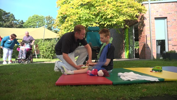 Ein Pfleger spielt mit einem Jungen im Garten. © NDR Foto: Christina Harland