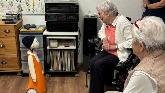 Zwei Seniorinnen sitzen in einem Pflegeheim vor einem Pflegeroboter. © NDR Foto: Jasmin Janosch