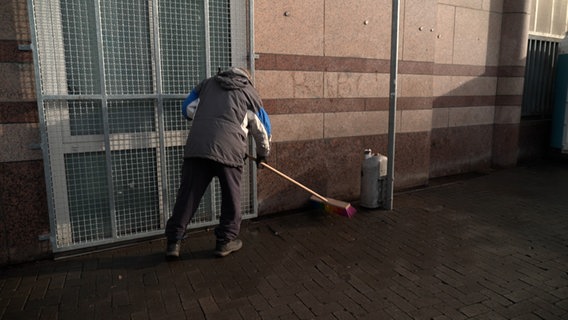 Ein Mann der Obdachlosen- und Drogenszene benutzt einen Besen zum Putzen. © NDR 