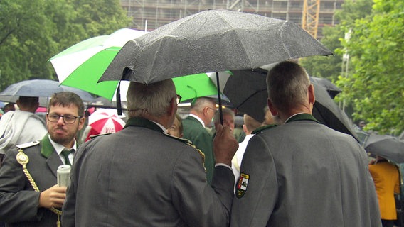 Teilnehmer des Schützenausmarsches in Hannover stehen unter einem Regenschirm. © NDR 