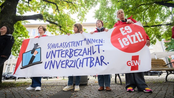 Schulassistentinnen und Schulassistenten demonstrieren mit einem Banner mit der Aufschrift "Schulassistent*innen. Unterbezahlt. Unverzichtbar" vor dem niedersächsischen Landtag. © picture alliance / dpa Foto: Jennifer Kramer