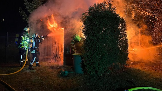 Zwei Feuerwehrleute unter Atemschutz versuchen, mit einem Schlauch einen brennenden Schuppen aus nächster Nähe zu löschen. © FFW Celle Foto: FFW Celle