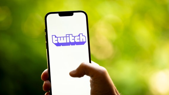 Eine Hand hält ein Smartphone in den Händen, auf dem Display ist das Twitch-Logo zu sehen. © picture alliance / NurPhoto Foto: Jaap Arriens