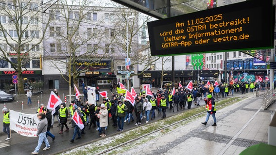 An einer Üstra-Haltestelle in Hannover wird auf einer Tafel über einen Streik informiert. Daneben laufen streikende Üstra-Mitarbeiter zu einer Demonstration. © dpa Foto: Julian Stratenschulte