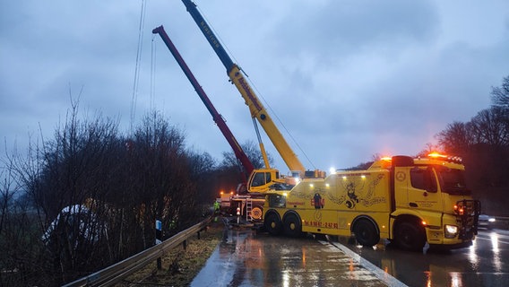 Zwei gelbe Schwerlastkräne heben mit Stahlseile einen weißen Lkw aus dem Graben neben der Autobahn. © Polizei Hildesheim 