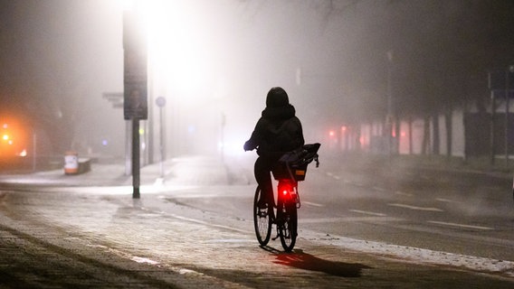 Eine Frau fährt am frühen Morgen in Hannover bei Nebel mit dem Fahrrad. © dpa Foto: Julian Stratenschulte