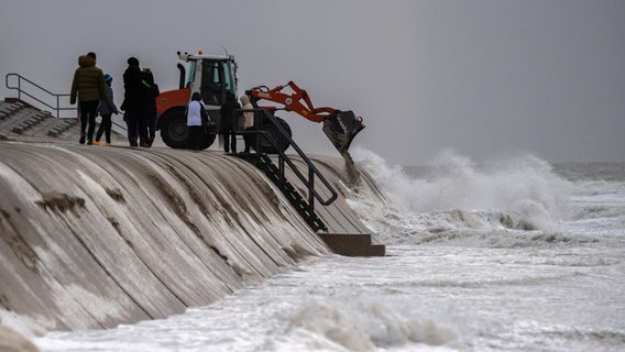 Mit einem Bagger wird während des Sturms der angewehte Sand von der Strandpromenade wieder in den Strand der Nordseeinsel Borkum gekippt. © picture alliance/dpa Foto: Mohssen Assanimoghaddam