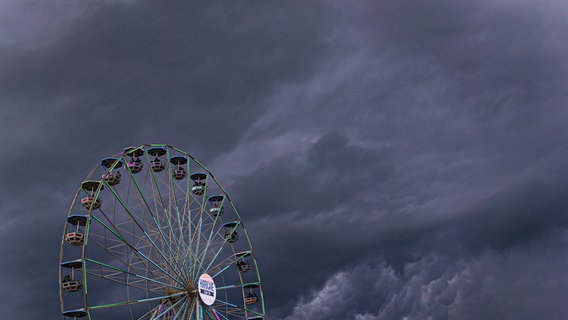 Dunkle Regenwolken ziehen über ein Riesenrad auf dem Gelände des Hurricane Festivals in Scheeßel hinweg. © dpa Foto: Moritz Frankenberg