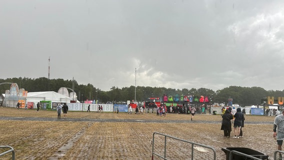 Zwei Festivalbesucher tragen Regenponchos, während dunkle Regenwolken über das Gelände des Hurricane Festivals in Scheeßel hinwegziehen. © NDR Foto: Thees Jagels