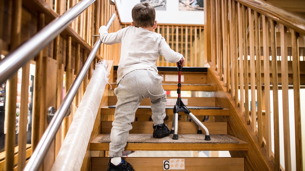 Ein Kind mit Gehhilfe geht in einer Kita eine Treppe hoch.