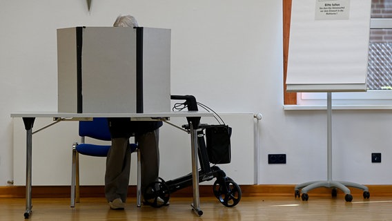 Eine Frau mit Rollator füllt in einer Wahlkabine ihren Stimmzettel zur Bundestagswahl aus. © dpa Foto: Swen Pförtner