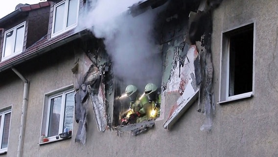 Einsatzkräfte der Feuerwehr schauen aus einem zerstörten Fenster in einem Mehrfamilienhaus in Langenhagen. © dpa +++ dpa-Bildfunk Foto: dpa +++ dpa-Bildfunk