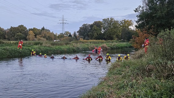 Die Einsatz·Kräfte von der DLRG laufen durch einen Fluss auf der Suche nach dem Vermissten Aurel S. DLRG ist die Abkürzung für Deutsche Lebens-Rettungs-Gesellschaft. © Polizeiinspektion Lüneburg/Lüchow-Dannenberg/Uelzen 