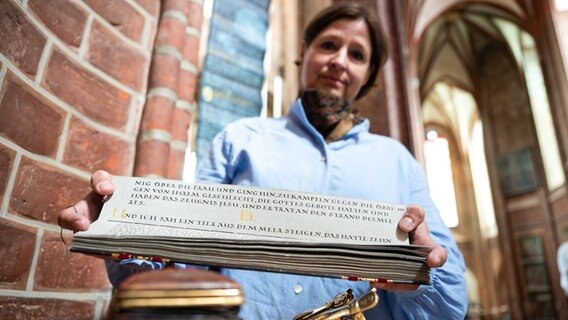 Antje Müller hält in der Kirche St. Nicolai von ihr mit Tintenfeder geschriebene Abschriften des Neuen Testaments in der Hand. © dpa-Bildfunk Foto: Philipp Schulze