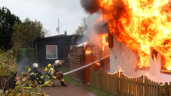 Zwei Feuerwehrmänner löschen mithilfe eines Löschschlauches ein komplett in Flammen stehendes Haus. © Feuerwehr Samtgemeinde Elbmarsch Foto: Lutz Wreide