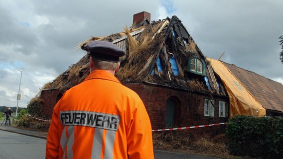 Ein Feuerwehrmann steht vor einem Reetdachhaus in Bütlingen. © NDR Foto: Marie-Elane Schulz