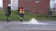 Feuerwehrleute in Buchholz neben einem Gulli, aus dem Wasser sprudelt. © Hellwig TV-Elbnews Produktion 