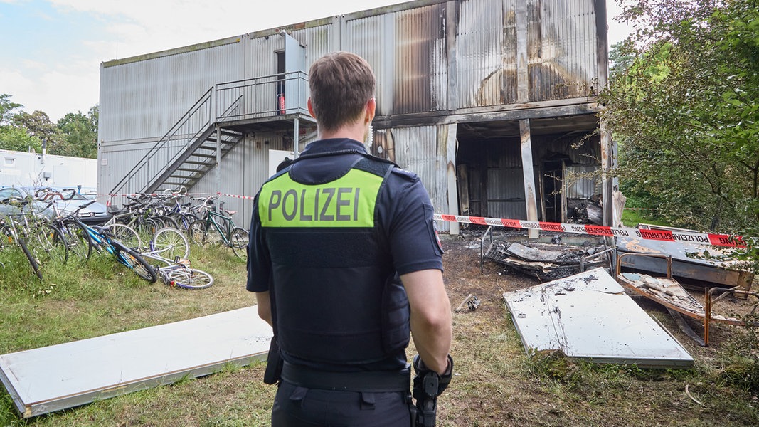 Ein Polizist steht vor einer abgebrannten Unterkunft für Geflüchtete.