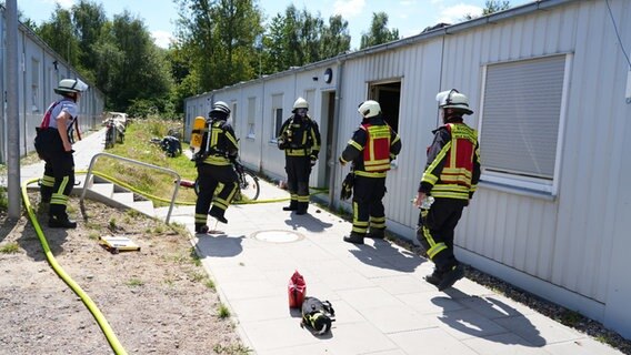 Einsatzkräfte der Feuerwehr stehen vor einer Flüchtlingsunterkunft aus Container in Buchholz. © JOTO Foto: JOTO