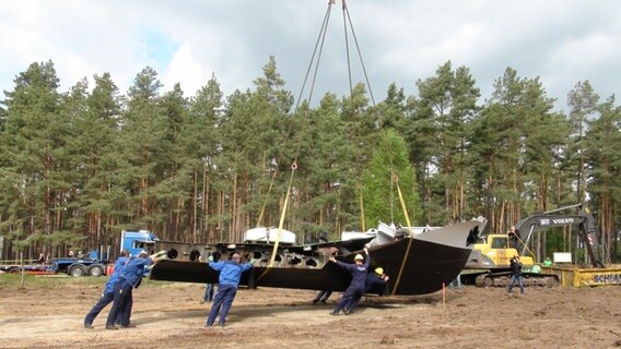 Mehrere Männer schieben ein, an einem Kran hängendes, Boot. © NDR Foto: Lars Gröning